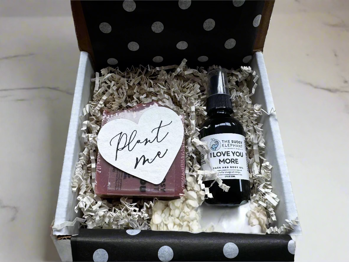 Gift box with a bottle of 'I Love You More' and a heart-shaped card on crinkled paper.
