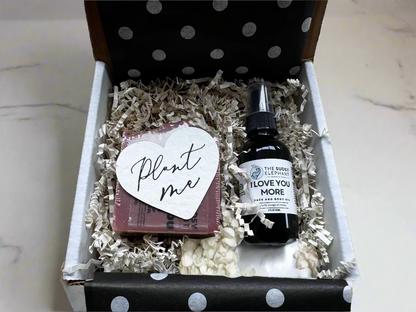 Gift box with a bottle of 'I Love You More' and a heart-shaped card on crinkled paper.